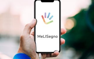 Logo dell'app MeLISegno: una manina con tre dita e la parte del palmo che somiglia ad un sorriso con i colori dell'arcobaleno. Sotto il nome dell'app.