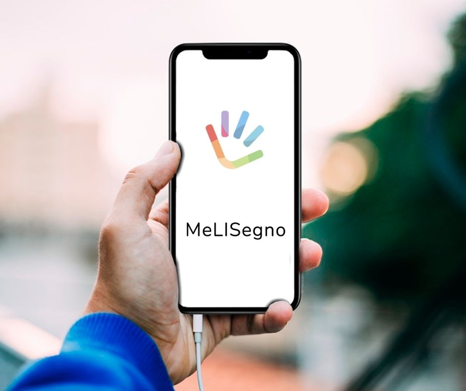 Logo dell'app MeLISegno: una manina con tre dita e la parte del palmo che somiglia ad un sorriso con i colori dell'arcobaleno. Sotto il nome dell'app.